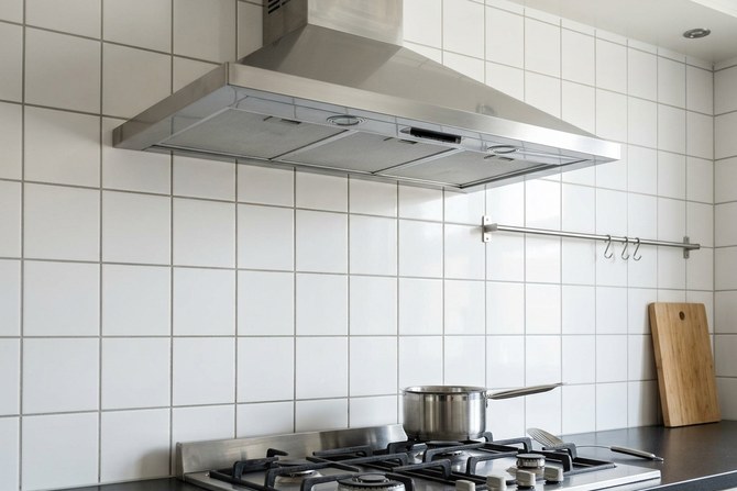 Bright stainless steel exhaust hood over a white tiled kitchen wall